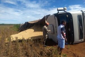 Caminhão cai em buraco, tomba e derrama 37 toneladas de farelo em estrada de chão
