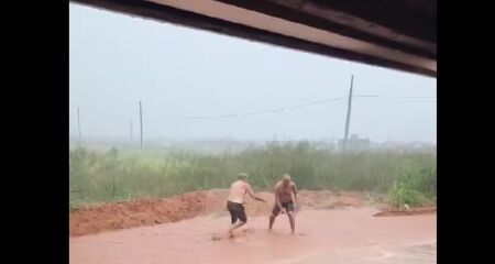 Cena descontraída em frente a um bar mostra dupla simulando luta de sumô durante tarde chuvosa no domingo