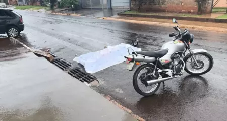 Corpo coberto com lençol ao lado de motocicleta