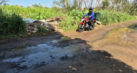 As margens da rua são tomadas por matagal e o local virou ponto de descarte de lixo e entulho