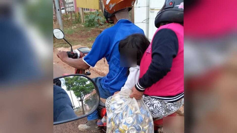Família carrega sacola de reciclável e criança sem capacete em moto